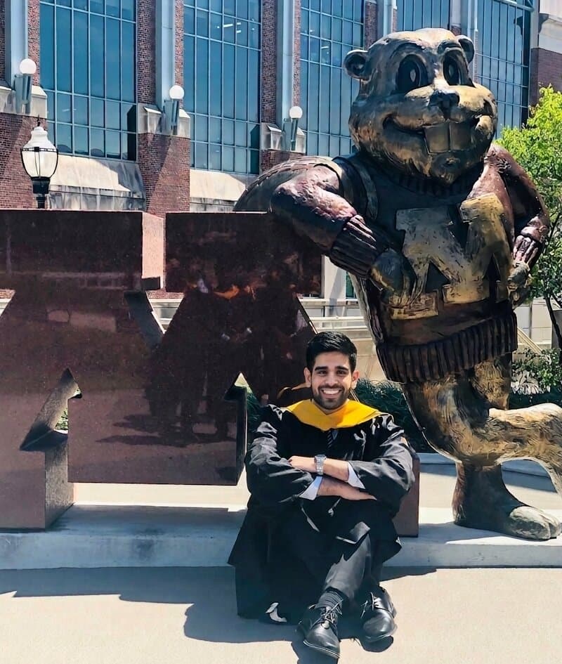 Sid Verma in a graduation gown in front of the block M and the Goldy statue at the University of Minnesota, 2019